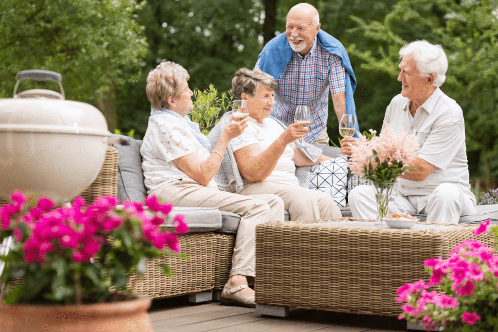 Two senior couples having a social gathering outside on a patio in the garden on summer afternoon.