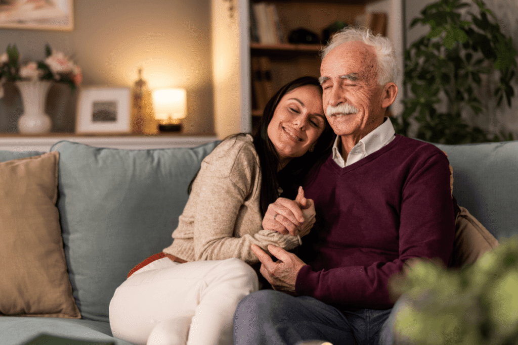Adult daughter having conversation with her senior father while they sitting on couch together in living room.